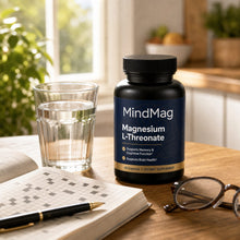 MindMag on a kitchen table beside a glass of water, a crossword and reading glasses